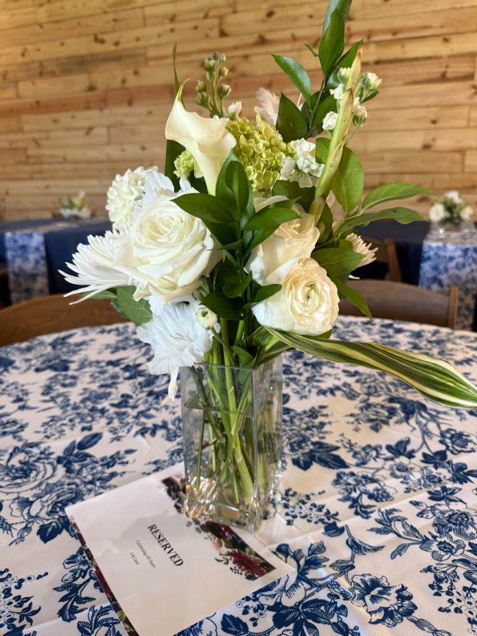 Mesa reservada con rosas blancas sobre un mantel floral azul
